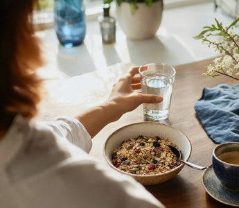 Wann Magnesium einnehmen: Person am Frühstückstisch greift nach einem Glas Wasser