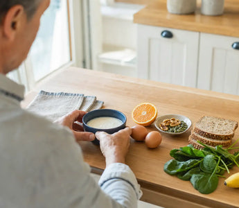 Magnesium kombinieren: Person bereitet in der Küche ein Frühstück mit Joghurt, Eiern, Nüssen und Obst vor