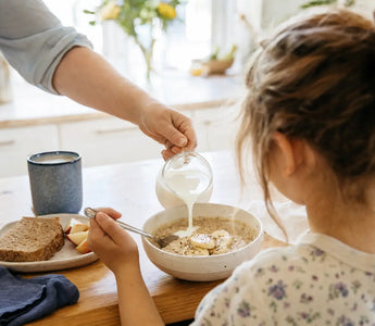 Magnesium für Kinder: Kind frühstückt Haferflocken mit Banane am hellen Küchentisch
