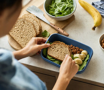 Wie viel Magnesium pro Tag: Person packt Vollkornbrot, Nüsse und Banane in eine Brotdose