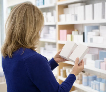 Magnesium Tabletten, Kapseln oder Pulver: Frau vergleicht in einer hellen Drogerie zwei schlichte Packungen